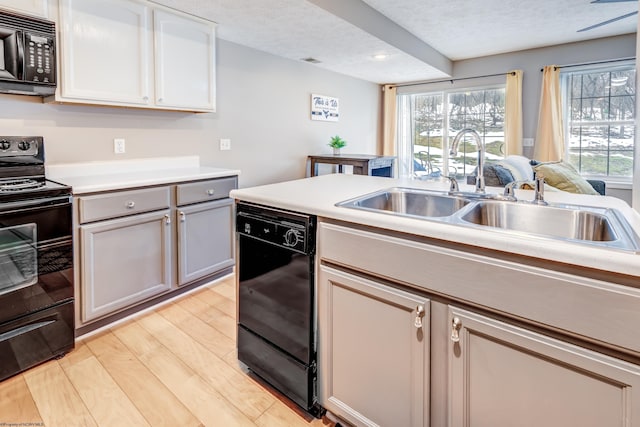 kitchen featuring sink, a textured ceiling, light wood-type flooring, and black appliances