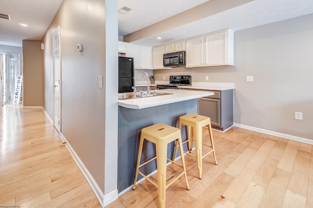 kitchen with a breakfast bar, sink, white cabinetry, light hardwood / wood-style flooring, and black appliances