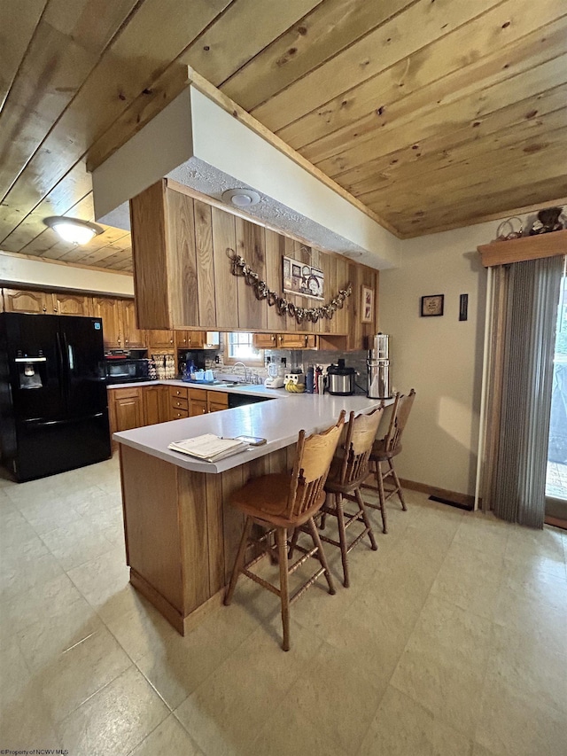 kitchen with wood ceiling, a breakfast bar area, kitchen peninsula, and black fridge