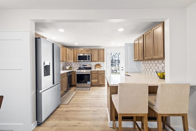 kitchen featuring stainless steel appliances, a kitchen bar, kitchen peninsula, and light hardwood / wood-style flooring