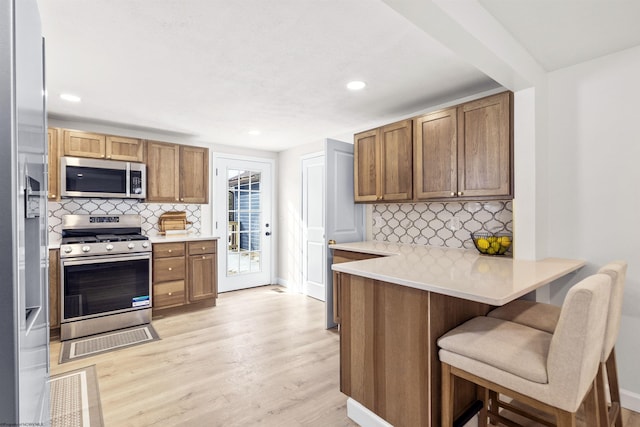 kitchen featuring light hardwood / wood-style flooring, a kitchen breakfast bar, kitchen peninsula, stainless steel appliances, and decorative backsplash