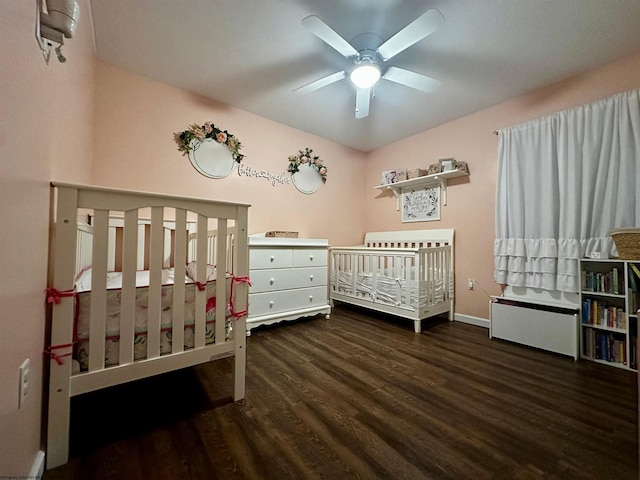 bedroom with dark wood-type flooring, a nursery area, and ceiling fan