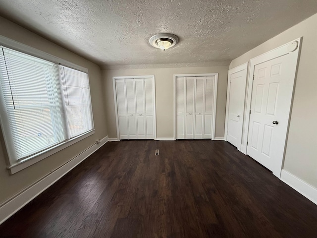 unfurnished bedroom with dark hardwood / wood-style flooring, a textured ceiling, and multiple closets