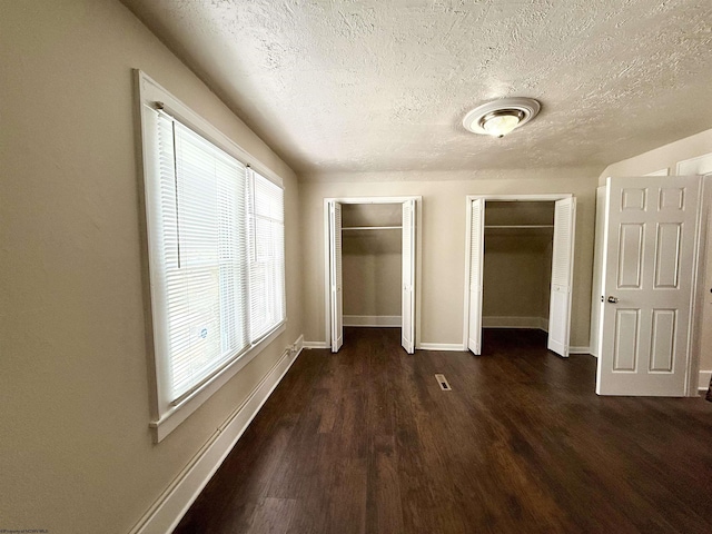 unfurnished bedroom featuring two closets, dark hardwood / wood-style floors, and a textured ceiling