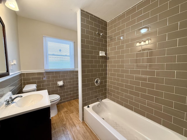 full bathroom with hardwood / wood-style flooring, tile walls, tiled shower / bath combo, vanity, and toilet