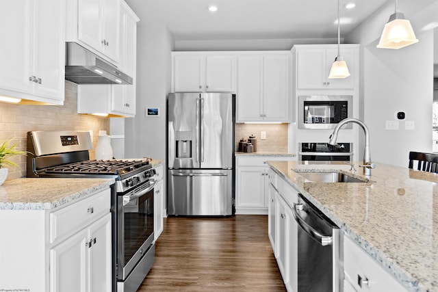 kitchen featuring sink, white cabinetry, light stone counters, appliances with stainless steel finishes, and pendant lighting