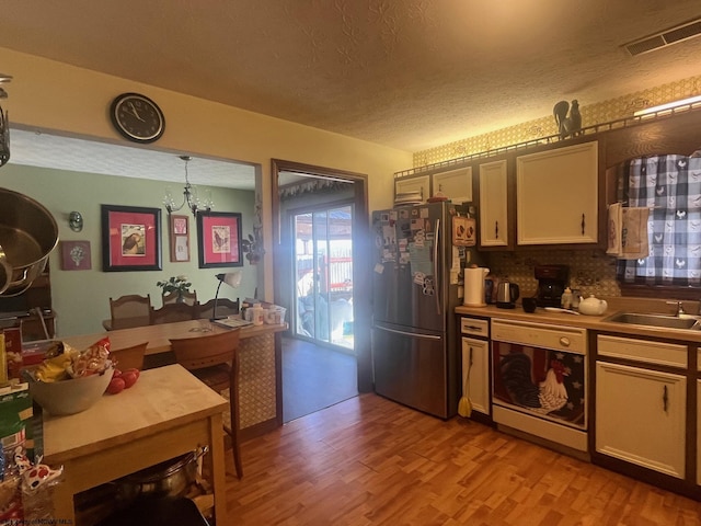 kitchen featuring sink, a textured ceiling, hanging light fixtures, light wood-type flooring, and stainless steel fridge