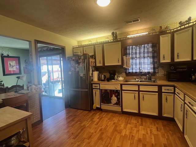 kitchen featuring stainless steel refrigerator, dishwasher, sink, light wood-type flooring, and a textured ceiling