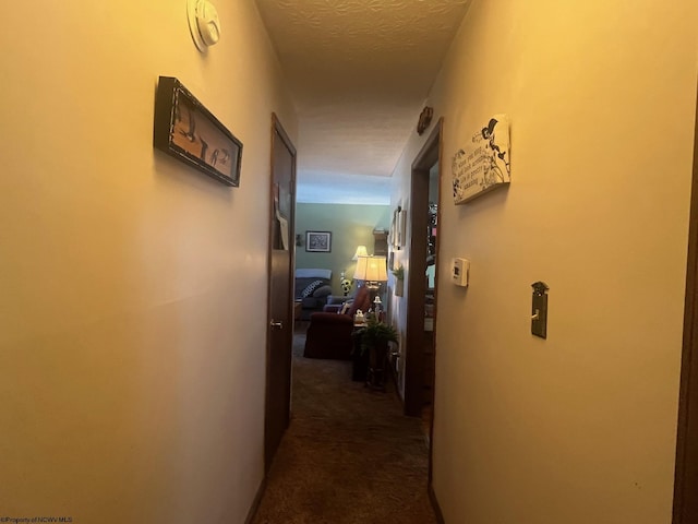 hallway featuring dark colored carpet and a textured ceiling