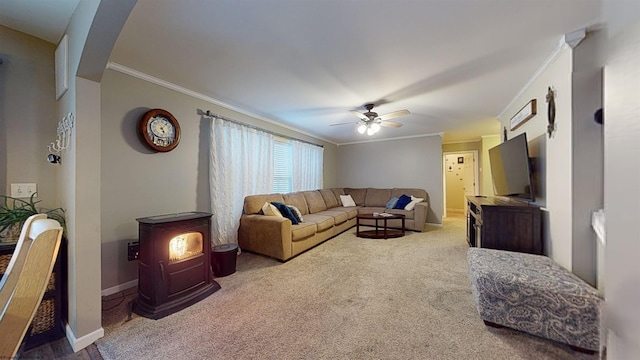 living room featuring ceiling fan, ornamental molding, carpet flooring, and a wood stove