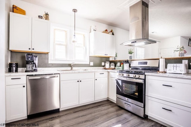 kitchen with appliances with stainless steel finishes, pendant lighting, island range hood, white cabinets, and a healthy amount of sunlight