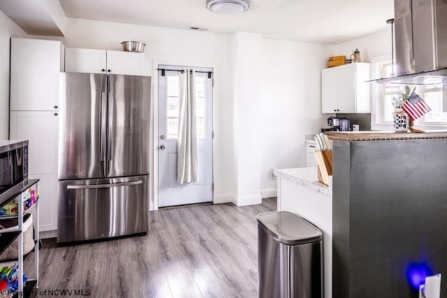 kitchen with stainless steel appliances, island range hood, white cabinets, and light hardwood / wood-style flooring