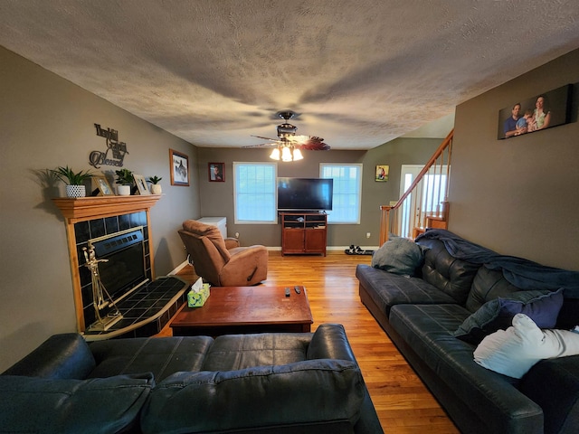 living room featuring ceiling fan, hardwood / wood-style flooring, a tile fireplace, and a textured ceiling