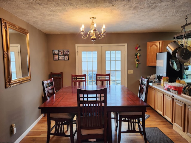 dining area with french doors, a chandelier, a textured ceiling, and light wood-type flooring