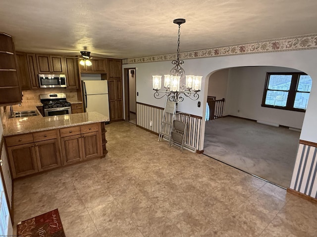 kitchen with sink, light stone counters, hanging light fixtures, appliances with stainless steel finishes, and kitchen peninsula