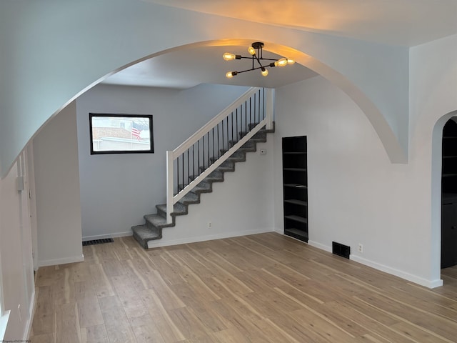 unfurnished living room with a notable chandelier and light hardwood / wood-style floors