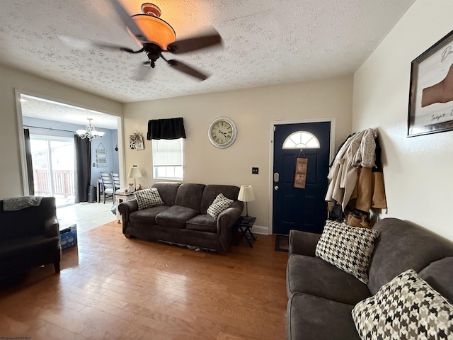 living room with ceiling fan with notable chandelier, light hardwood / wood-style flooring, and a textured ceiling