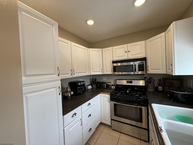 kitchen with light tile patterned flooring, appliances with stainless steel finishes, sink, and white cabinets