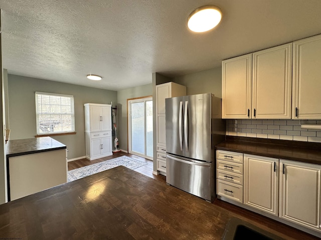 kitchen with dark hardwood / wood-style flooring, backsplash, stainless steel refrigerator, and white cabinets