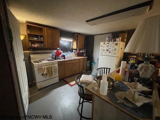 kitchen featuring white appliances, concrete flooring, a breakfast bar, and sink