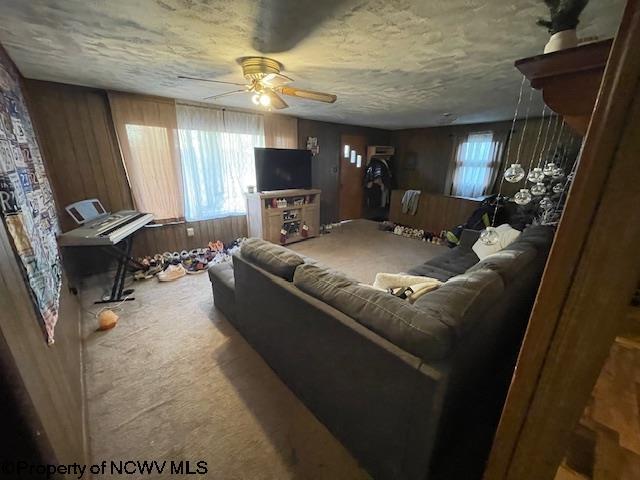 carpeted living room featuring a textured ceiling, ceiling fan, and wood walls