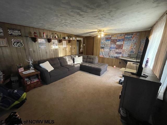 carpeted living room featuring ceiling fan and wooden walls