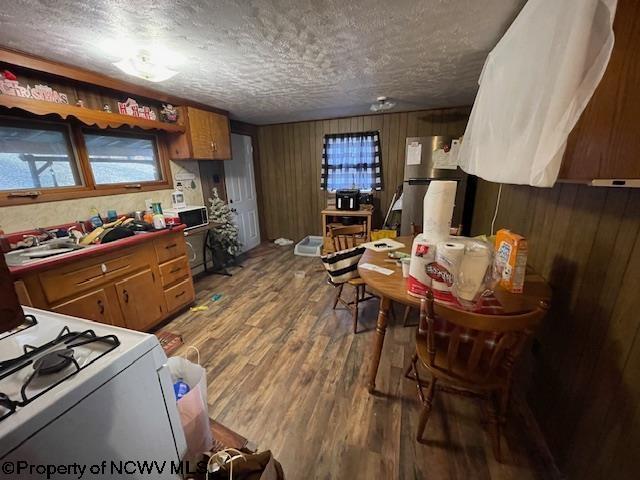 kitchen featuring white gas stove, wood walls, a textured ceiling, stainless steel refrigerator, and hardwood / wood-style floors