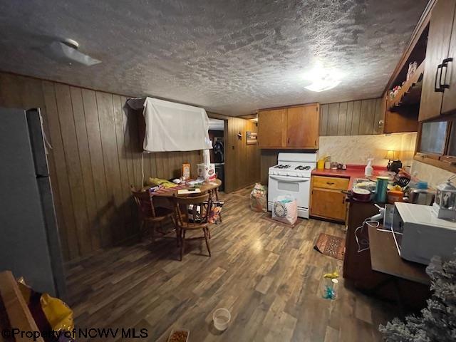 kitchen featuring gas range gas stove, wood walls, a textured ceiling, fridge, and dark hardwood / wood-style flooring