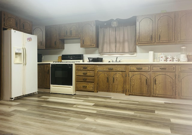 kitchen featuring sink, white refrigerator with ice dispenser, range with gas stovetop, and light wood-type flooring