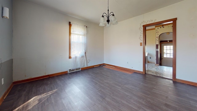 empty room featuring dark wood-type flooring, a chandelier, and a healthy amount of sunlight