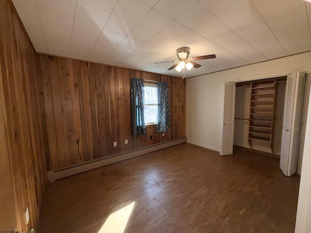 unfurnished bedroom featuring hardwood / wood-style floors, wooden walls, ceiling fan, baseboard heating, and a closet