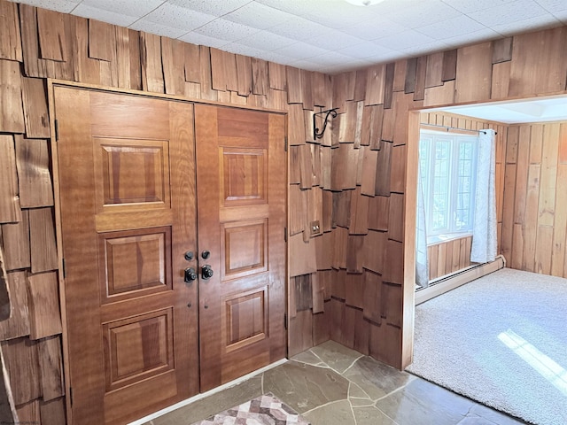 foyer entrance with a baseboard radiator, carpet, and wood walls