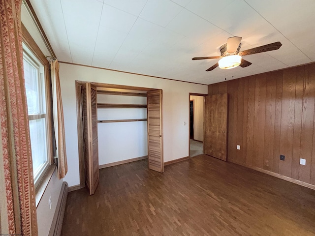 unfurnished bedroom featuring dark hardwood / wood-style flooring, ornamental molding, ceiling fan, a baseboard radiator, and wooden walls