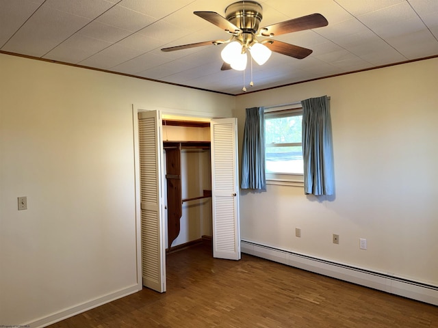 unfurnished bedroom with ceiling fan, baseboard heating, wood-type flooring, ornamental molding, and a closet