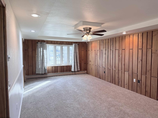 carpeted spare room featuring baseboard heating, ceiling fan, wood walls, and a textured ceiling