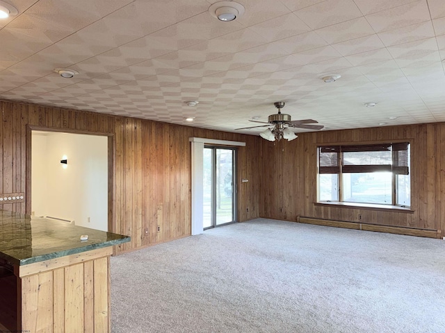 carpeted spare room featuring ceiling fan, a baseboard radiator, and wood walls