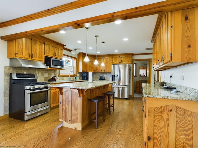 kitchen with light wood-type flooring, ornamental molding, appliances with stainless steel finishes, a kitchen island, and light stone countertops