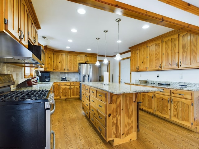 kitchen with sink, appliances with stainless steel finishes, hanging light fixtures, light stone countertops, and a kitchen island