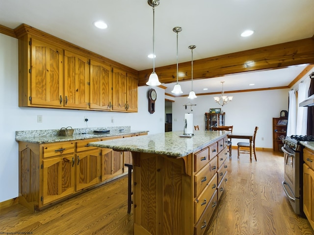 kitchen featuring stainless steel gas range oven, light stone counters, a center island, hanging light fixtures, and light wood-type flooring