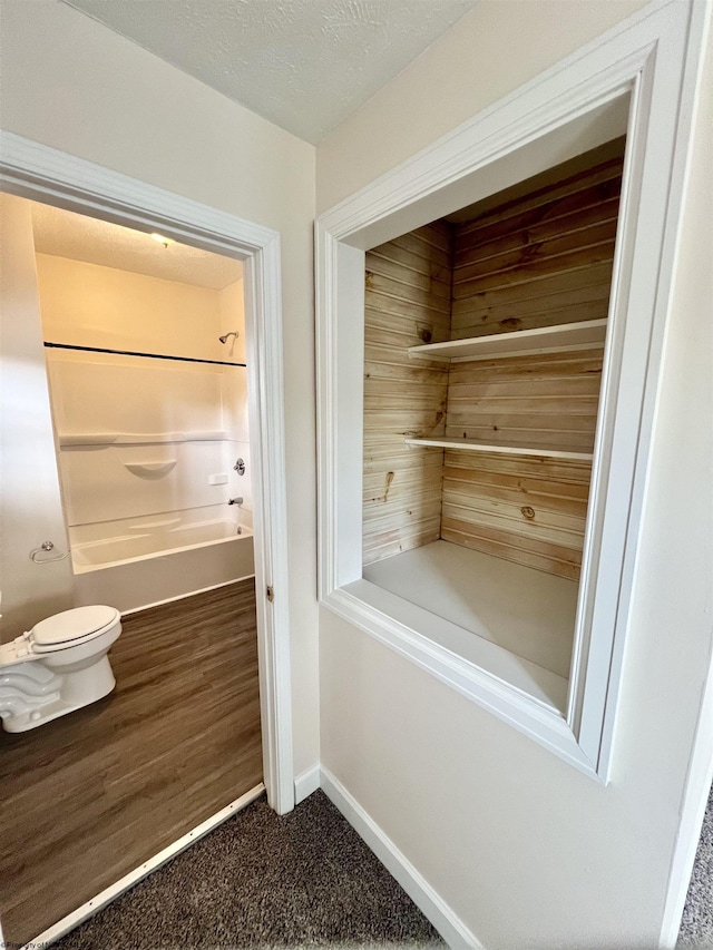 interior space with bathing tub / shower combination, a textured ceiling, and toilet