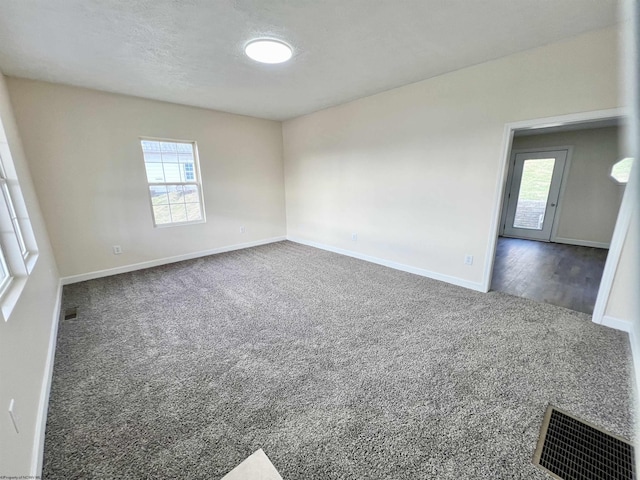 spare room with dark carpet, a textured ceiling, and a wealth of natural light