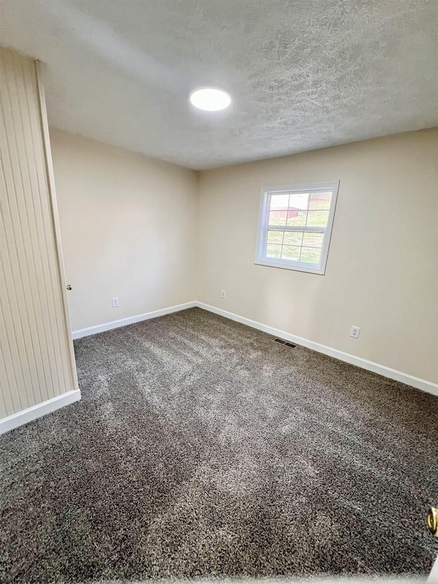 spare room featuring dark colored carpet and a textured ceiling