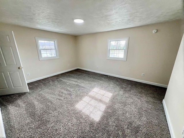 spare room with dark carpet, a wealth of natural light, and a textured ceiling