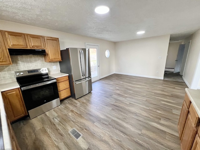 kitchen featuring decorative backsplash, light hardwood / wood-style flooring, stainless steel appliances, and a textured ceiling