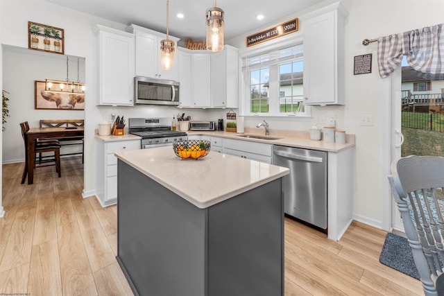 kitchen featuring a kitchen island, appliances with stainless steel finishes, sink, white cabinets, and hanging light fixtures