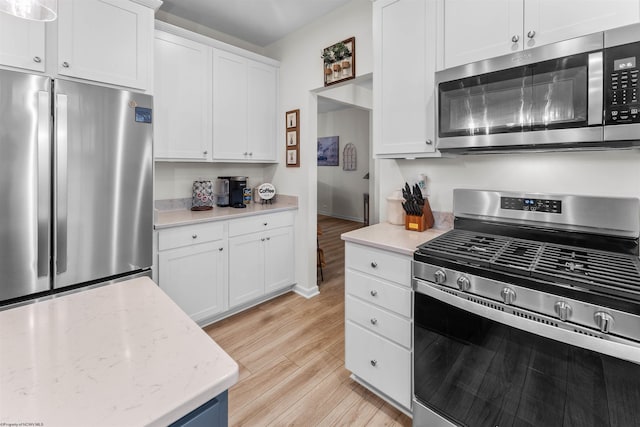 kitchen with light stone countertops, appliances with stainless steel finishes, white cabinets, and light hardwood / wood-style floors