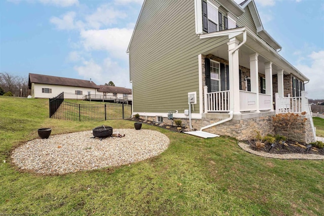 view of side of property with an outdoor fire pit, a yard, and covered porch