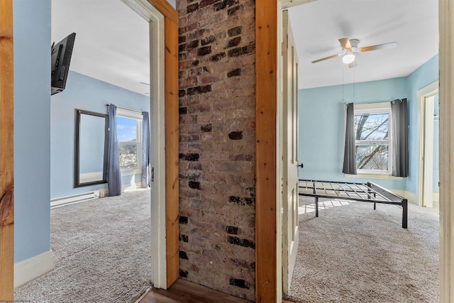 hallway featuring a baseboard radiator, brick wall, and carpet