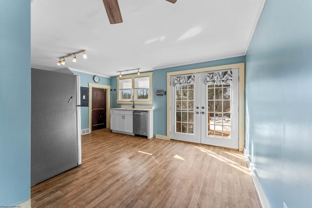 kitchen with appliances with stainless steel finishes, french doors, white cabinets, ornamental molding, and light hardwood / wood-style flooring