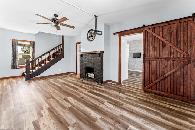 unfurnished living room featuring hardwood / wood-style flooring, ceiling fan, a barn door, and a brick fireplace